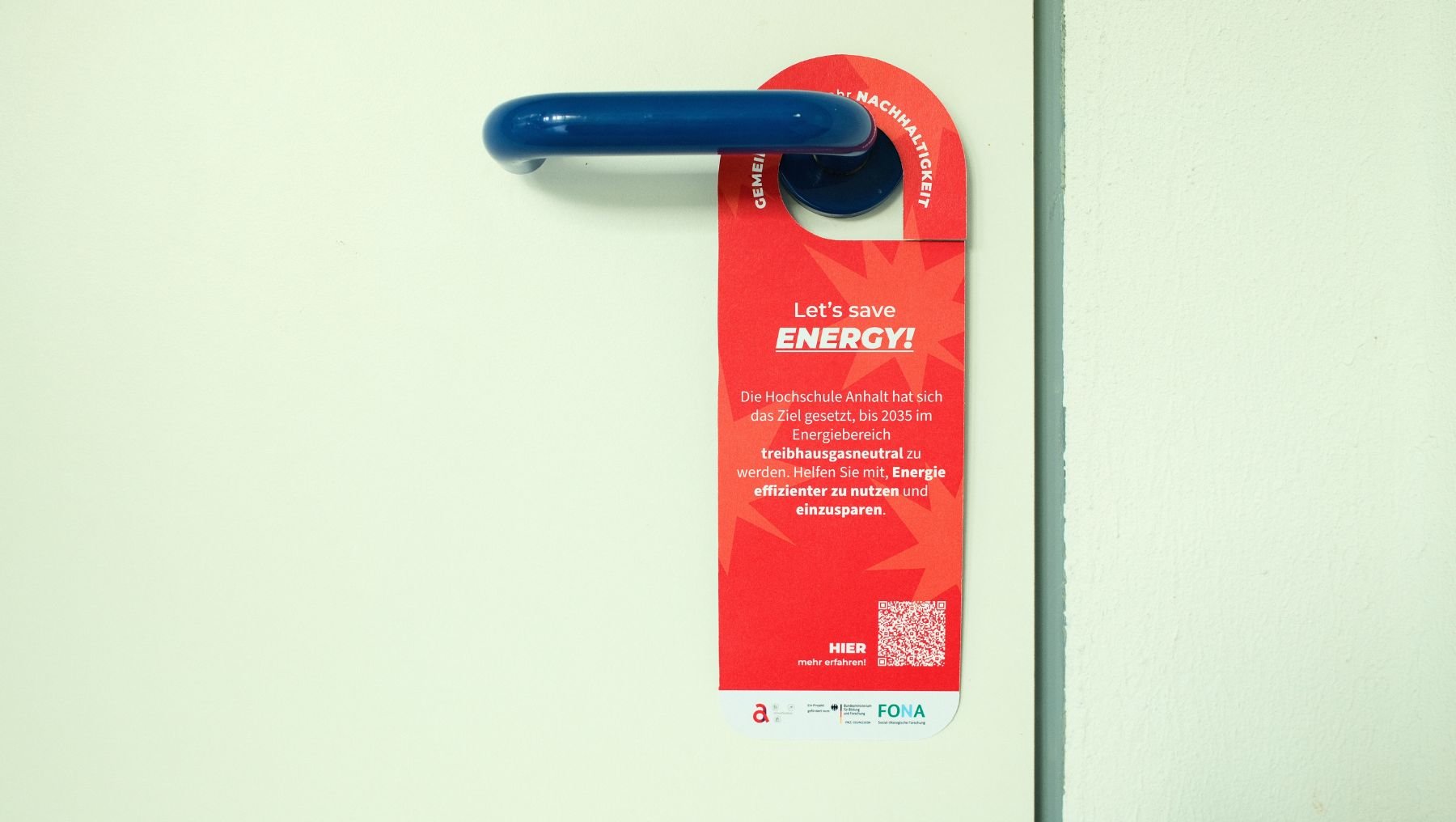 Foto zeigt roten Türanhänger mit Aufdruck zum Energiesparen an der Hochschule Anhalt