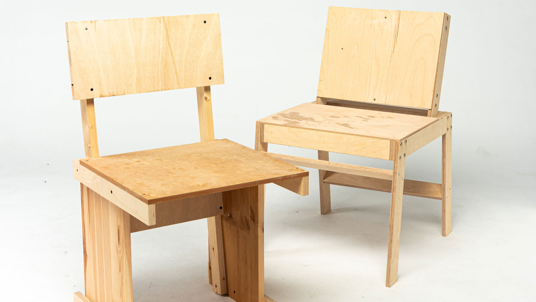 Zwei einfache Holzbänke mit flachen Sitzflächen und Rückenlehnen aus unbehandeltem Holz, die aneinandergefügt sind.