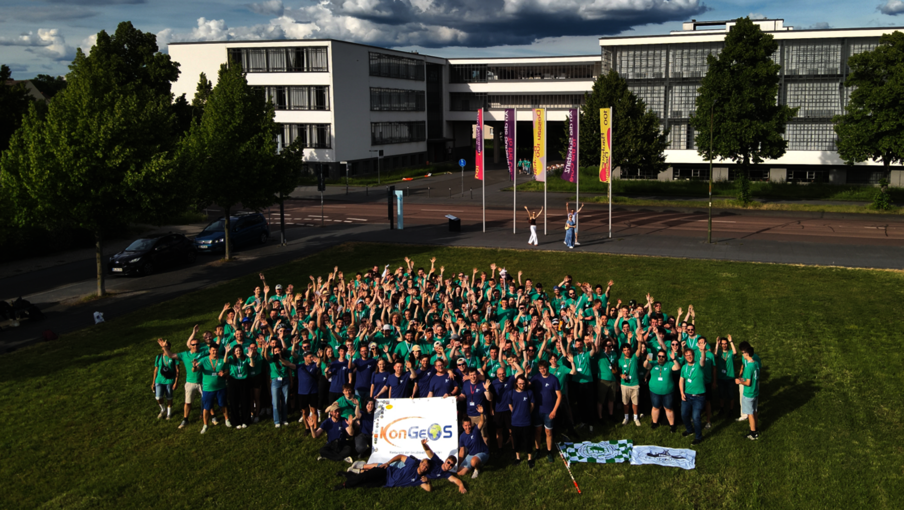 Große Gruppe von Menschen in grünen T-Shirts, die auf einem Rasen vor einem Gebäudekomplex posiert, einige halten ein Schild mit dem Logo „Copernicus“. Drei Flaggen im Hintergrund.
