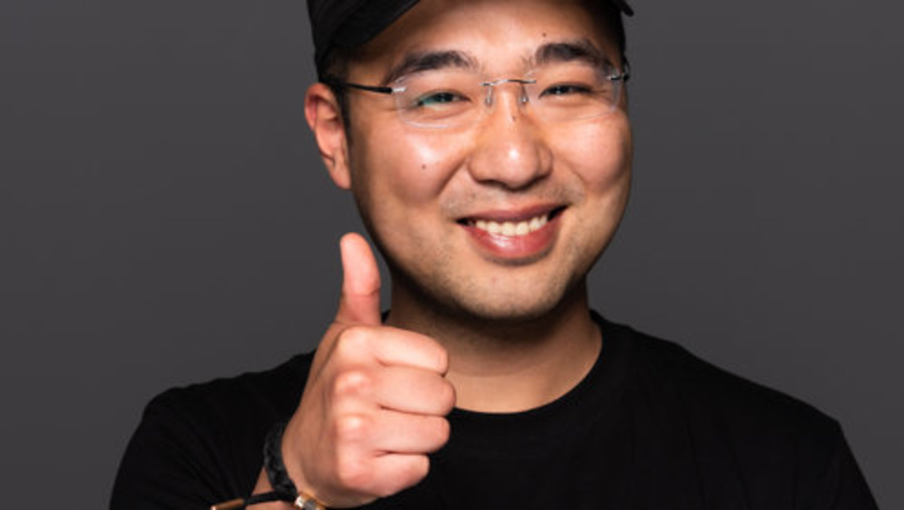Lächelnder Mann mit Brille und schwarzer Basecap gibt mit Daumen hoch ein positives Feedback, trägt ein schwarzes T-Shirt mit dem Aufdruck "Richmond".