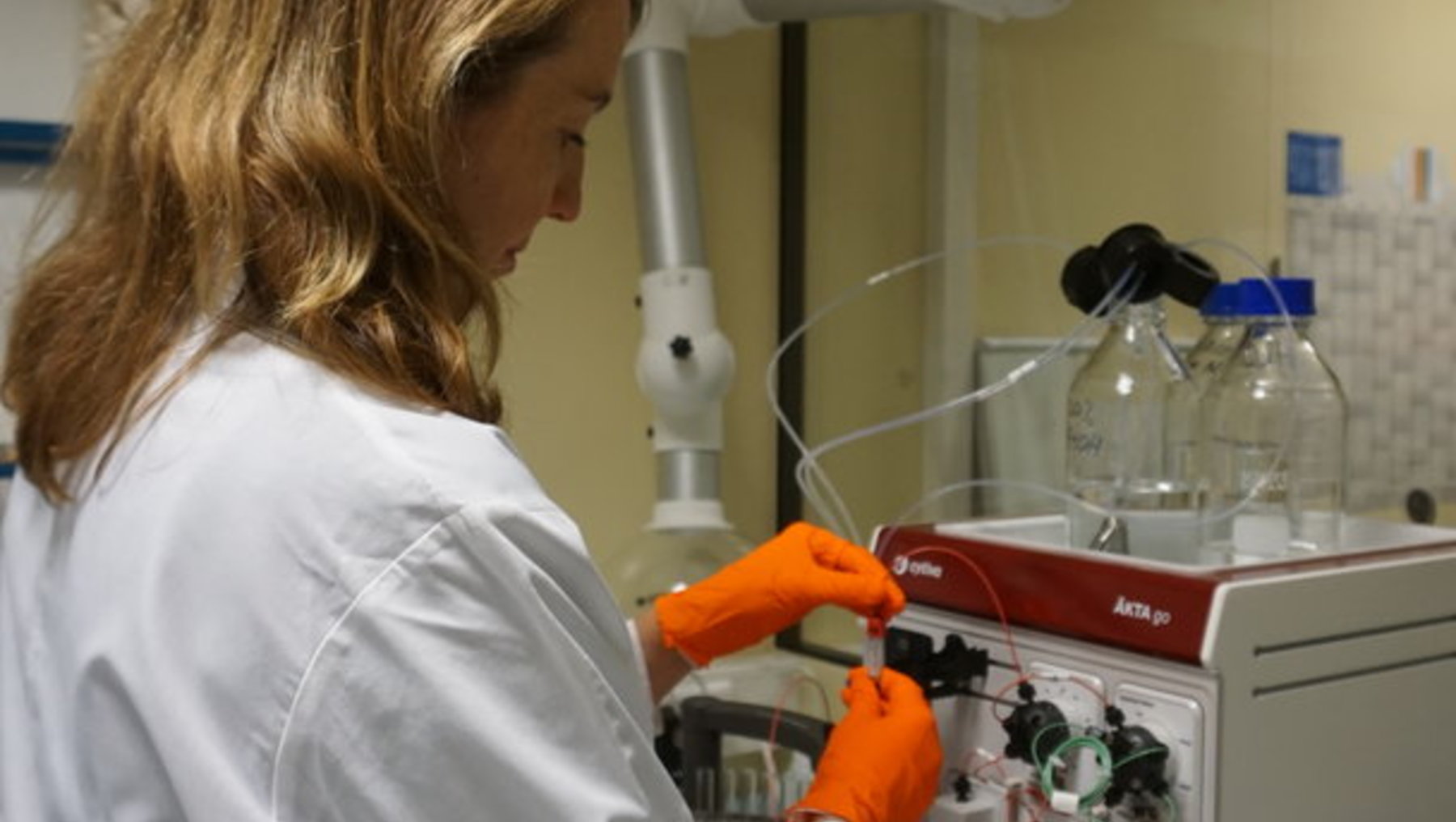 Eine Laborantin in weißem Kittel und Handschuhen bedient ein analytisches Gerät, vermutlich ein Gaschromatograph oder Massenspektrometer, und führt präzise Messungen oder Analysen durch.