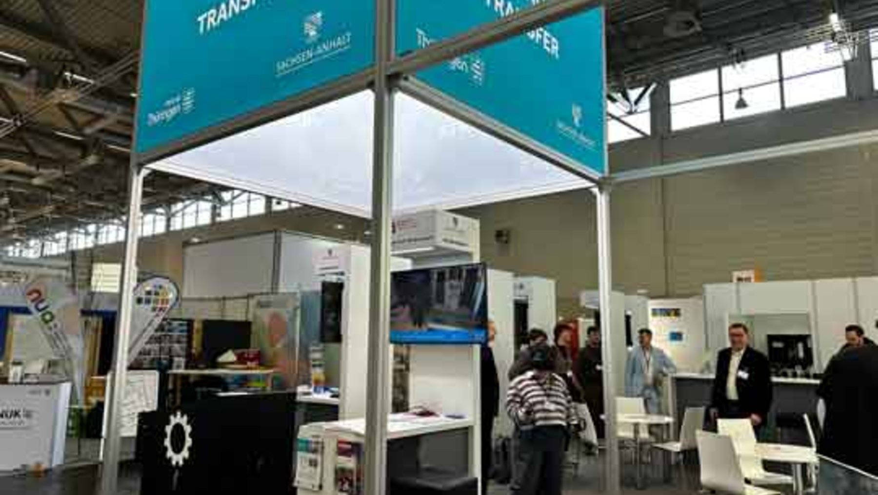 Ausstellungstand mit dem Thema „Innovation, Science, Transfer“ auf der Hannover Messe, an dem mehrere Personen stehen und sich unterhalten. Im Hintergrund weitere Messestände und Besucher.