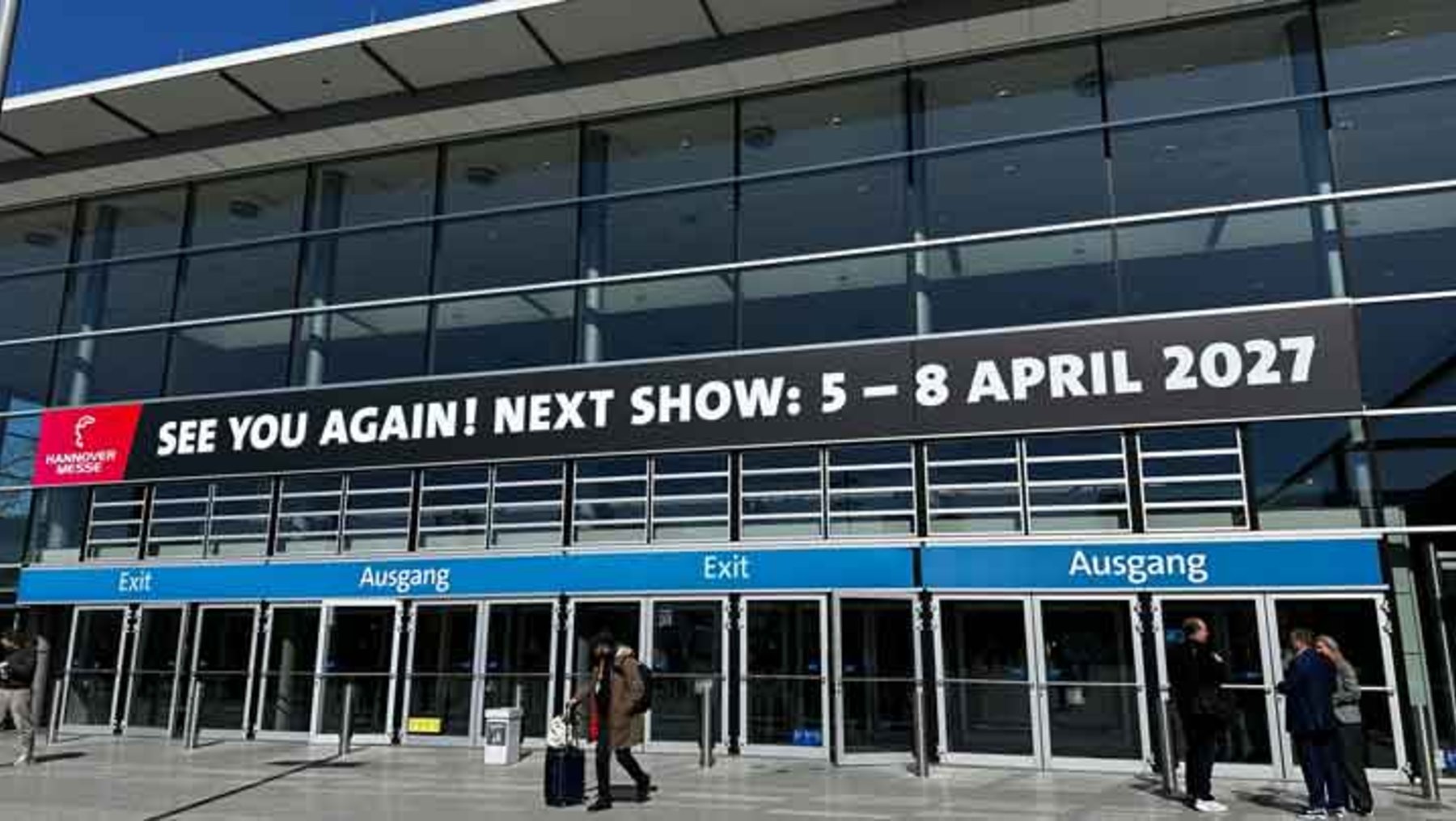 Einladung zur nächsten Messe mit Datum vom 5. bis 8. April 2027, vor einem gläsernen Messeeingang mit Ausgängen und Besuchern.